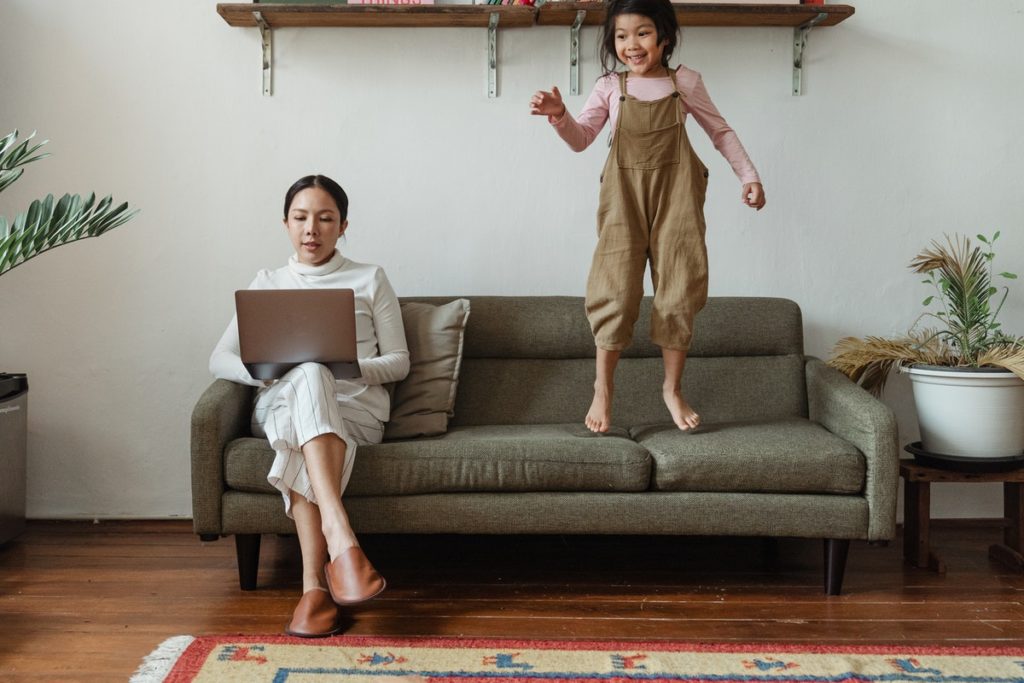 woman working from home with daughter jumping on the sofa