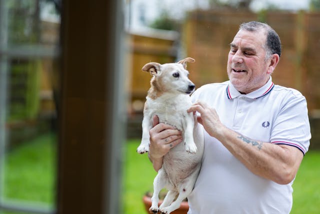 Elderly Man in Polo Shirt Holding Dog in Hands
